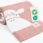 Rosa Babydecke aus Baumwolle zusammengerollt mit GOTS- und OEKO-TEX-Anhänger – hochwertige, nachhaltige baby decke baumwolle als gestrickte Kuscheldecke fürs Baby.