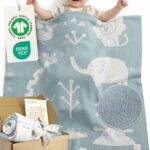 Glückliches Baby liegt unter blauer Babydecke aus Baumwolle mit Tiermotiven, GOTS- und OEKO-TEX-zertifizierte Babydecke von Merle Toys; weiche gestrickte Decke fürs Baby, ideales Geschenk zur Geburt oder Taufe mit Karte – Perfekt geeignet als Baby Meilenstein Decke.