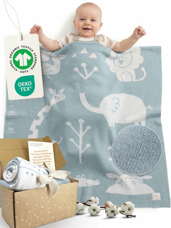 Glückliches Baby liegt unter blauer Babydecke aus Baumwolle mit Tiermotiven, GOTS- und OEKO-TEX-zertifizierte Babydecke von Merle Toys; weiche gestrickte Decke fürs Baby, ideales Geschenk zur Geburt oder Taufe mit Karte – Perfekt geeignet als Baby Meilenstein Decke.