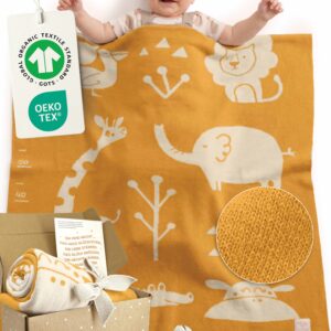 Glückliches Baby liegt unter Babydecke aus Baumwolle in Gelb – gestrickte Babydecke für Kinderwagen, aus zertifizierter Bio-Baumwolle, ideales Geschenk zur Geburt Mädchen und Jungen. GOTS- und OEKO-TEX-zertifiziert mit Geschenkverpackung + Karte.
