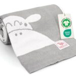 Grau-weiße gestrickte Babydecke aus Baumwolle, zusammengerollt mit OEKO-TEX und GOTS Anhänger – hochwertige Bio Baumwolle Babydecke, ideal als Meilenstein Decke für Babys.