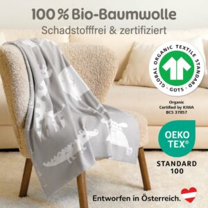 Weiche graue Babydecke aus Baumwolle über einem Sessel drapiert, zertifiziert nach GOTS und OEKO-TEX – nachhaltige Bio Baumwolle Babydecke und moderne gestrickte Babydecke.
