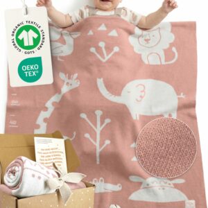 Glückliches Baby liegt unter rosa Babydecke aus Baumwolle. GOTS- und OEKO-TEX-Anhänger – hochwertige, nachhaltige Baby Decke Baumwolle als gestrickte Kuscheldecke fürs Baby. Mit Geschenkverpackung und Karte.