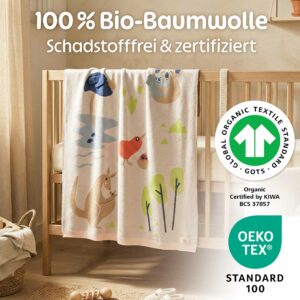 Die Merle Toys Baumwoll Babydecke Savannenfreunde hängt am Babybett und zeigt, dass die Bio Babydecke aus 100 Prozent Bio-Baumwolle besteht, schadstofffrei und zertifiziert ist.