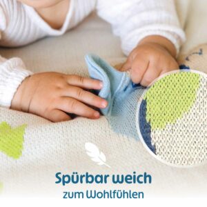 Kleine Babyhände greifen nach dem weichen 3D-Element der Merle Toys Baumwoll Babydecke, während die Bio Babydecke Savannenfreunde ihre weiche Strickstruktur zeigt.