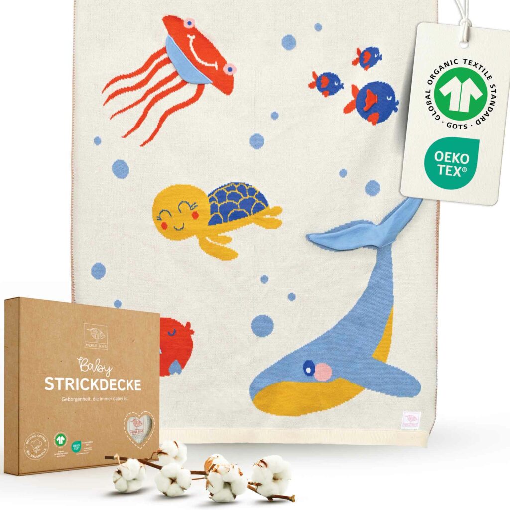 Merle Toys Baumwoll Babydecke im liebevollen Meereswelt-Design mit Wal, Schildkröte, Fischen und Qualle. Die gestrickte Babydecke wird in einer Geschenkbox mit Grußkarte geliefert und eignet sich dadurch wunderbar als Geschenk zur Taufe Mädchen. Dank Bio-Baumwolle, GOTS- und OEKO-TEX-Zertifizierung ist die gestrickte Babydecke Sommer wie auch ganzjährig eine weiche, sichere Wahl für Babys.