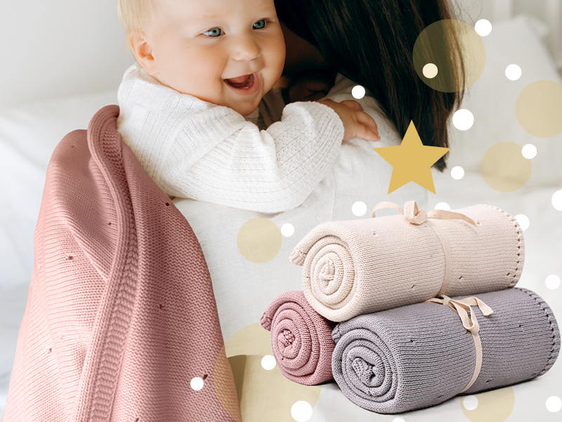 Weihnachtsgeschenke für Kinder – Baby im Arm mit kuscheliger Strickdecke in Rosa, ideal als Geschenk.