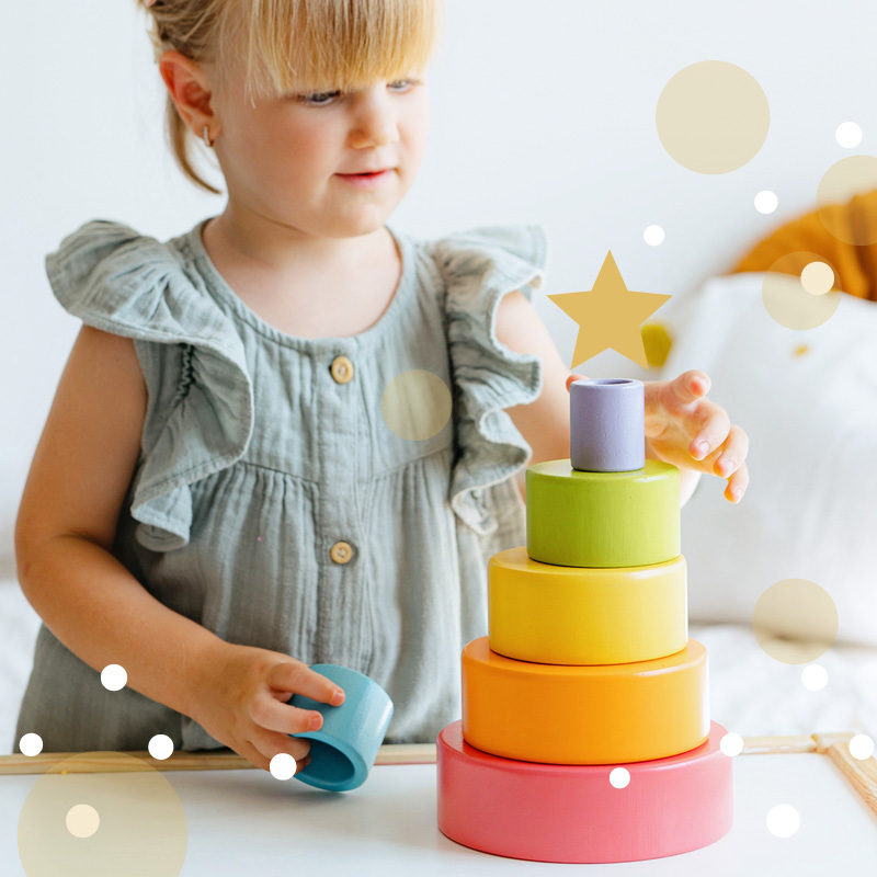 Weihnachtsgeschenke für Kinder – Mädchen stapelt bunte Stapelbecher, nachhaltiges Lernspielzeug für die Kleinsten.
