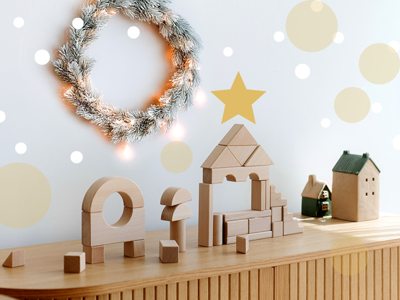 Weihnachtsgeschenke für Kinder – kreative Bauideen mit Holzbausteinen, festlich inszeniert neben Tannenkranz und Häuschen