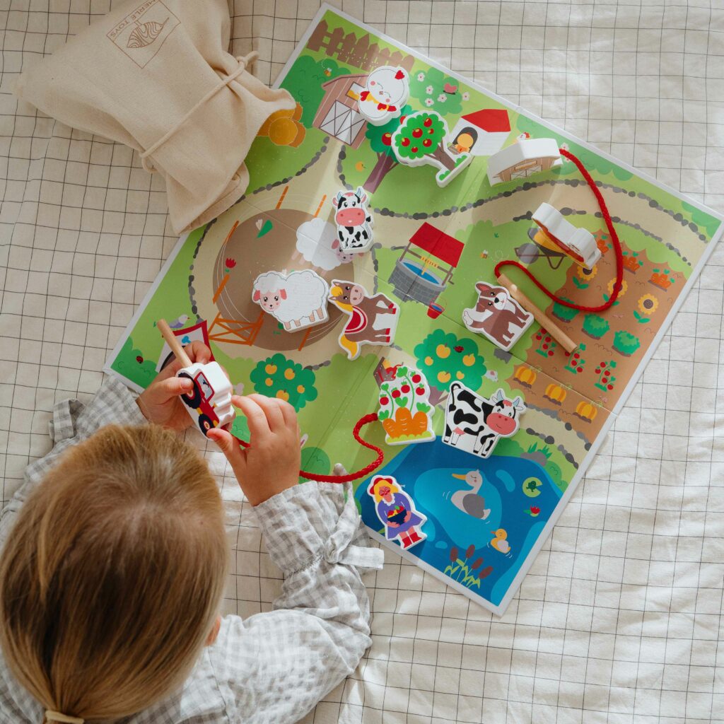 Kind spielt mit einem Bauernhof-Fädelspiel aus Holz – ein lernförderndes und spielerisches Set, perfekt für Geschenke für 2-Jährige. Das hochwertig illustrierte Spiel ist ein sinnvolles Geschenk für 2-Jährige und eignet sich wunderbar als Weihnachtsgeschenk für ein Kind mit 2 Jahren.