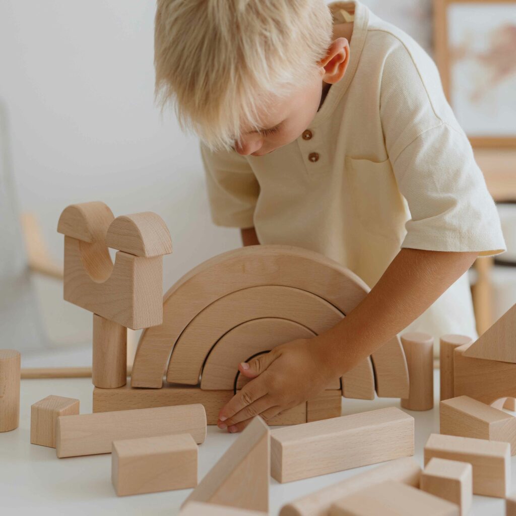 Junge baut konzentriert mit hochwertigen Holzbausteinen und Regenbogen-Elementen – ein klassisches Motorikspielzeug und ideales Geschenk für 2-Jährige. Perfekt als sinnvolles Geschenk für 2-Jährige für Jungs & Mädchen sowie als nachhaltiges Weihnachtsgeschenk für 2-Jährige.