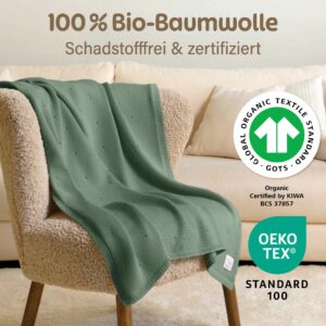Merle Toys_Bio Baumwoll Babydecke Strick aus  100% Bio Baumwolle liegt drapiert auf einem beigen Sessel. Unsere Decke Baby ist schadstofffrei, zertifiziert, kuschelig und hautfreundlich.
