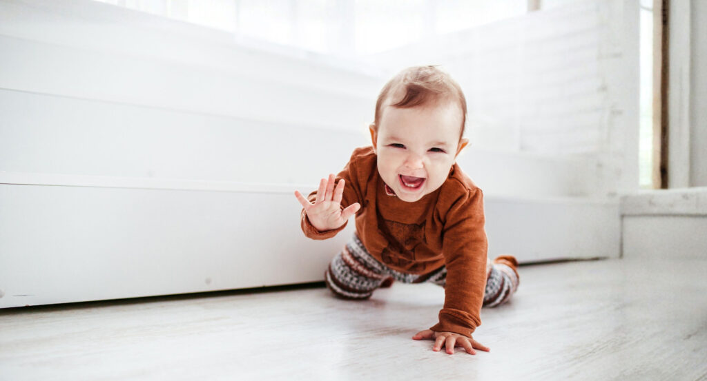 Kleines Kind krabbelt fröhlich auf dem Boden und lacht in die Kamera.