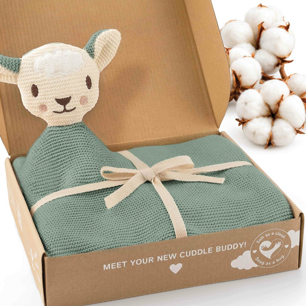 Geöffnete Geschenkbox mit der grünen Merle Toys_Knuddeldecke, süßem Schafsköpfchen und dekorativen Baumwollblüten. Die Baby Kuscheldecke ist eine gestrickte Babydecke Grün aus Baumwolle und eignet sich als weiche Babydecke Baumwolle und Kuscheldecke für Babys.