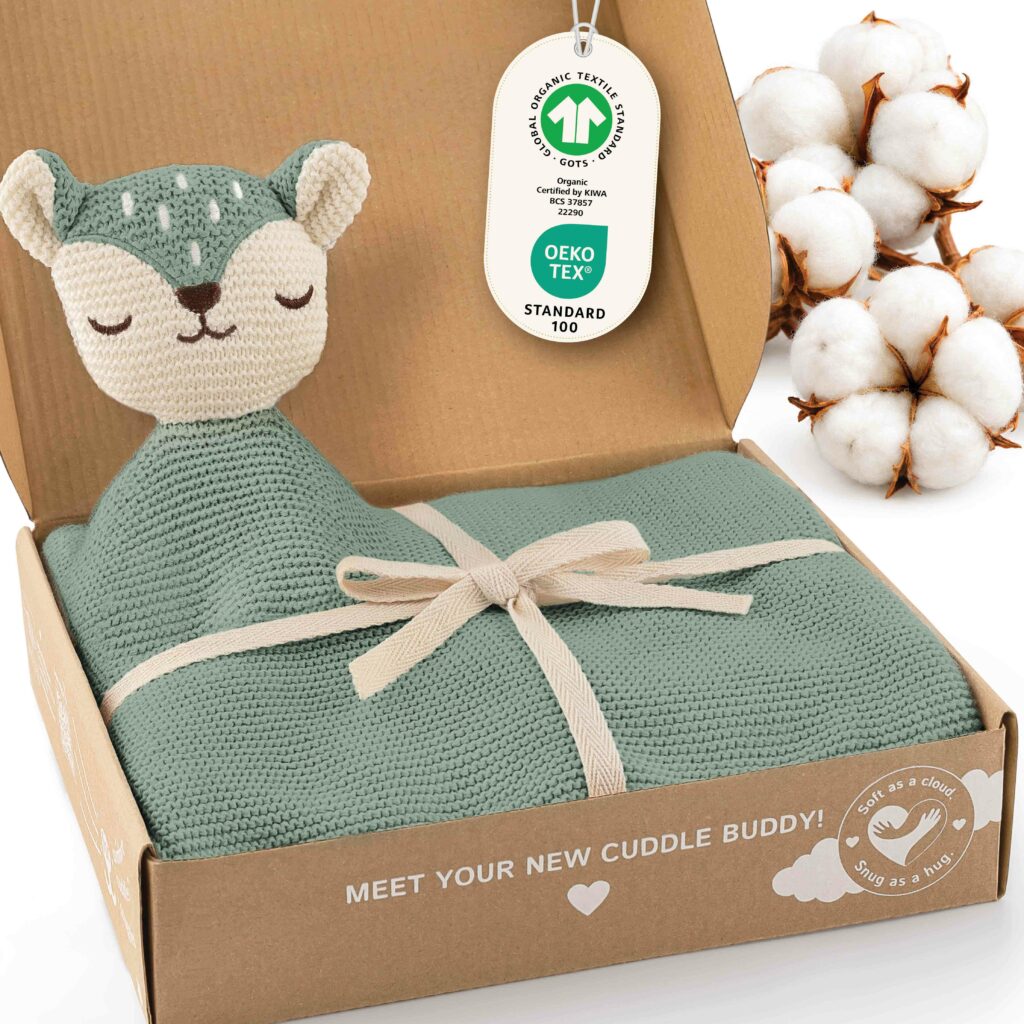 Geöffnete Geschenkbox mit der grünen Merle Toys Knuddeldecke, integriertem Fuchsköpfchen, Schleife sowie GOTS und OEKO TEX Kennzeichnung. Die Baby Kuscheldecke ist eine gestrickte Babydecke Grün aus Baumwolle und eignet sich als weiche Babydecke Baumwolle und Kuscheldecke für Babys.