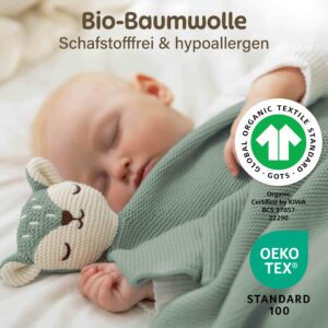 Ein schlafendes Baby liegt zugedeckt mit der grünen Merle Toys Knuddeldecke und kuschelt neben dem weichen Fuchsköpfchen. Die Baby Kuscheldecke wird mit GOTS und OEKO TEX Zertifizierung gezeigt und eignet sich als gestrickte Babydecke Grün, Babydecke Baumwolle und Kuscheldecke für Babys.