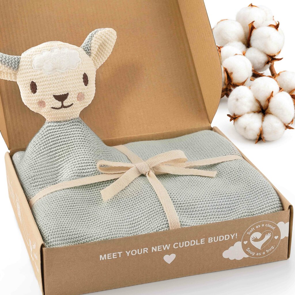 Geöffnete Geschenkbox mit der mintfarbenen Merle Toys_Knuddeldecke, süßem Schafsköpfchen, Schleife und dekorativen Baumwollblüten. Die weiche Kuscheldecke für Babys ist eine gestrickte Baby Decke für Neugeborene aus Baumwolle und eignet sich als Kinderwagen Decke, Baumwolldecke, Babydecke Winter und Geschenk zur Geburt Mädchen.